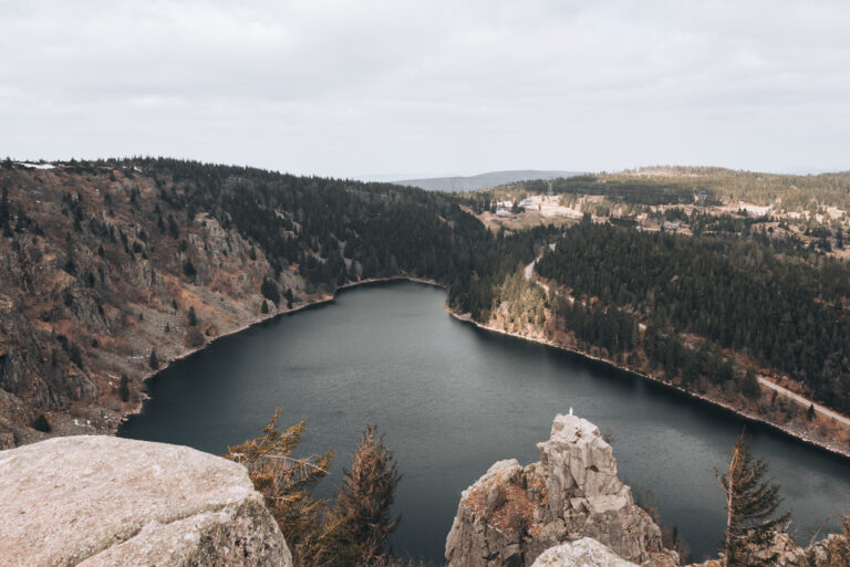 Panorama of the Lac Blanc from the Observatoire Belmont. The lake is surrounded by tree covered hills.