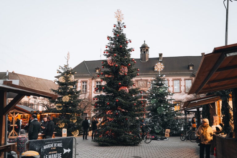 Three Christmas trees covered in lights are surrounded by wooden chalets in Place Joffre at the Christmas market in Thann.