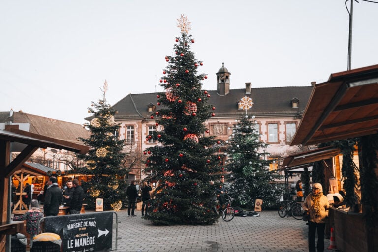 Three Christmas trees stand in Thann's Place Joffre lit with twinkling lights and surrounded by wooden huts at during the Christmas Market.