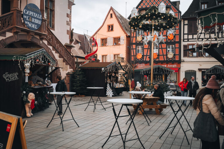 This iPlace de la Victoire at the Sélestat Christmas Market. There are tables and wooden chalets selling food and crafts.