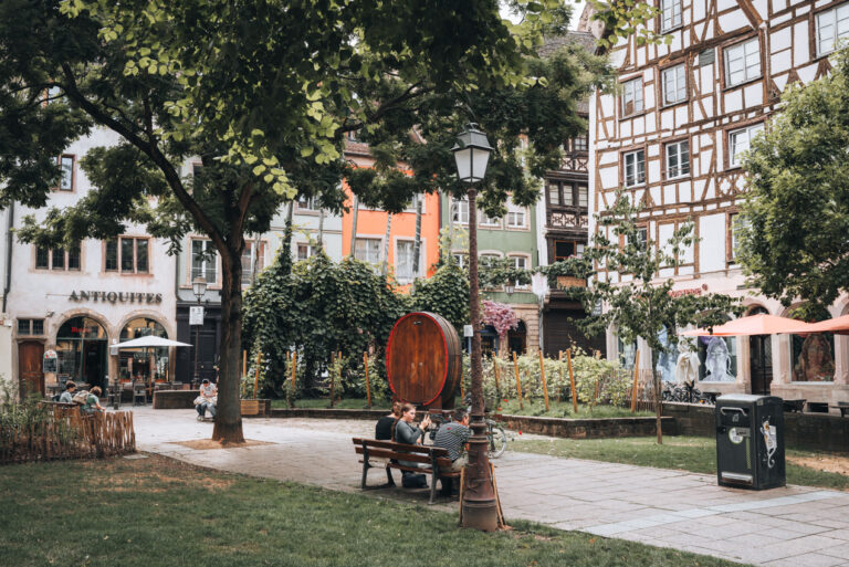 Place des Tripiers in summer with people sitting on benches enjoying the scenery. This is one of the stops along the Guided Walking Tour in Strasbourg between History and Curiosities.