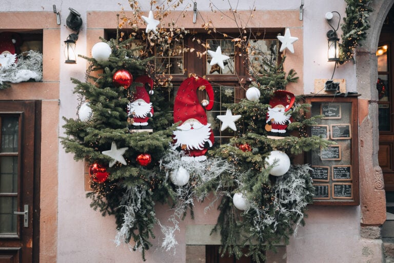 This is a window that is decorated for the Riquewihr Christmas market. There is a Santa, several wreaths, and ornaments.