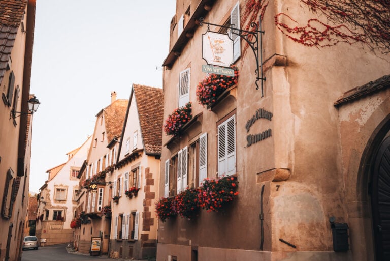 Rue Principale in the Alsatian wine village of Mittelbergheim lined with historic houses and colorful flower boxes hanging from balconies. The quiet street reflects the traditional charm of villages along the Alsace Wine Route.