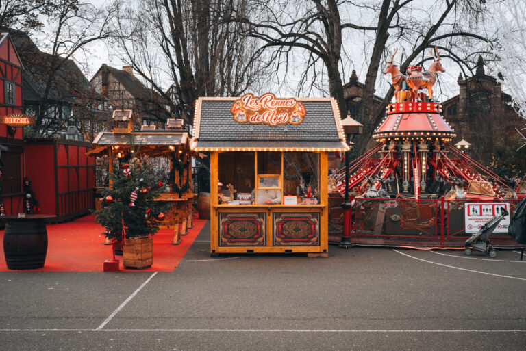 A wooden chalet and a carousel are decorated with lights and ornaments along Rue de la Montagne Verte in Colmar at Christmas.
