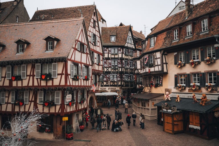 This is Rue des Marchands at the Colmar Christmas Market. THere are half-timbered buildings decorated with festive ornaments and lights.