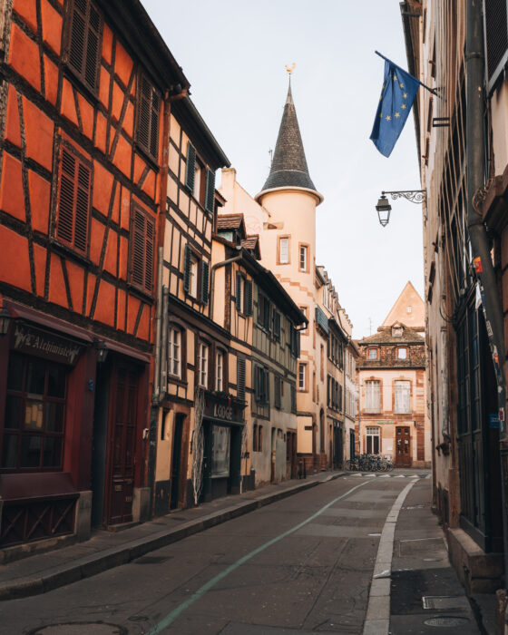 Quiet cobblestone street of Rue des Sœurs in Strasbourg bathed in soft golden sunrise light, with historic buildings casting long shadows across the empty road. The peaceful morning atmosphere highlights the charm of old town streets in Strasbourg.