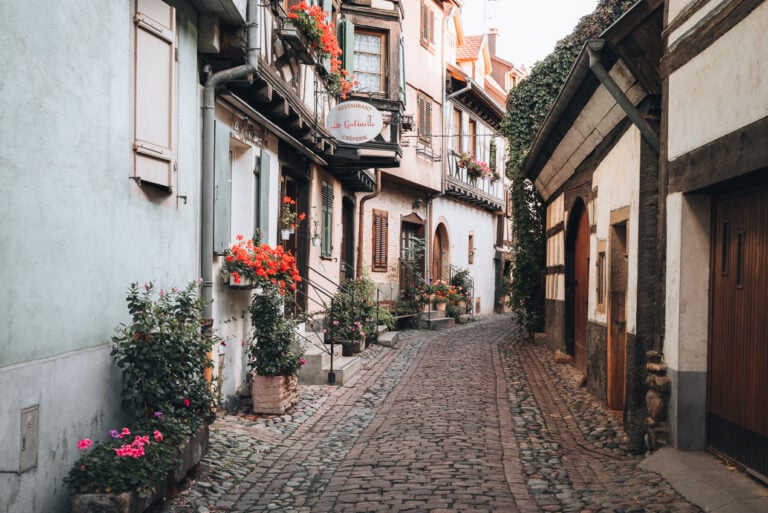 This is Rue du Rempart. It's a cobblestone street lined with colorful half-timbered houses. There are hanging baskets of colorful houses on the windowsills.