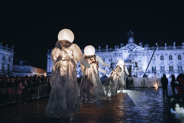 This is the Saint Nicolas Day Parade in Nancy. It's in Place Stanislas and there are lights on the Hôtel de Ville and there are people dressed in costumes.