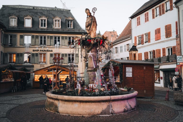 Saint Theobald Fountain in Thann decorated with lights, ornaments, and wreaths for the Christmas market.