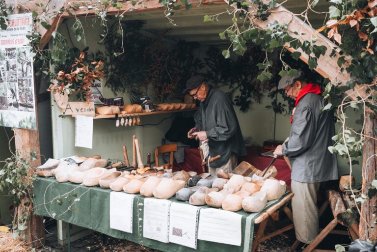 A shoemaker at work cobbling a wooden shoe. There are rows of wooden shoes in front of him that he has already made.