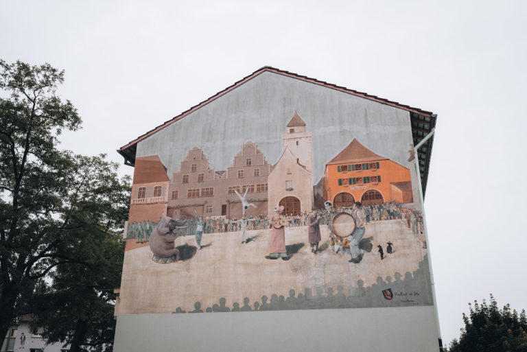 Street Art of a a city with people playing in the center. It's on the side of an apartment building at the corner of Boulevard des Alliés and Rue de la Mutualité in Mulhouse.