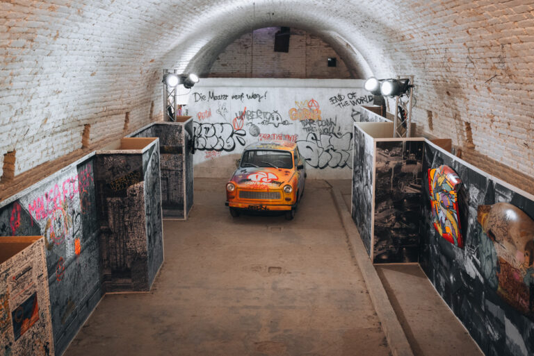 A spray-painted car surrounded by painting from local artists inside the Vauban Fortificaitons in Neuf-Brisach.