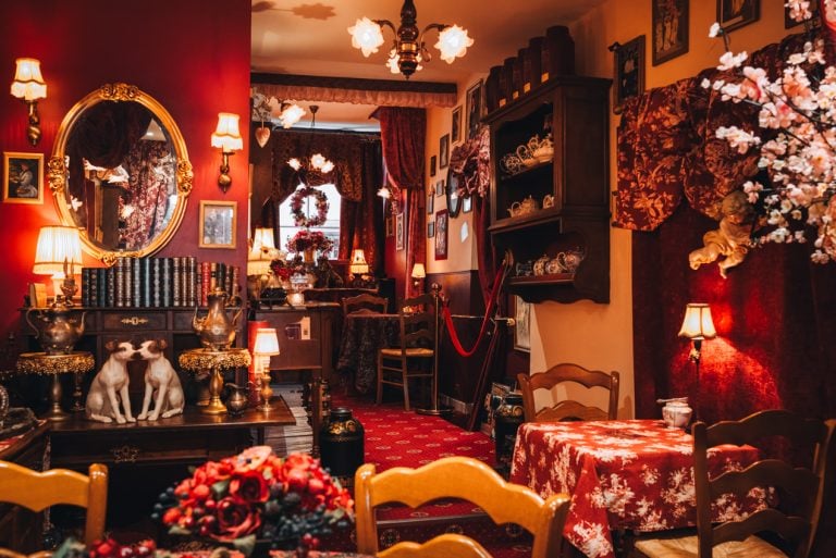 This is the tearoom at Au Fond du Jardin. There are tables, chairs, teapots, and books on a bookshelf.