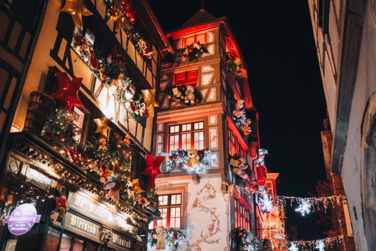 Historic Strasbourg building decorated with oversized teddy bears, garlands, and festive holiday displays during the Christmas market season. The whimsical decorations make this one of the city's most photographed sights in December.