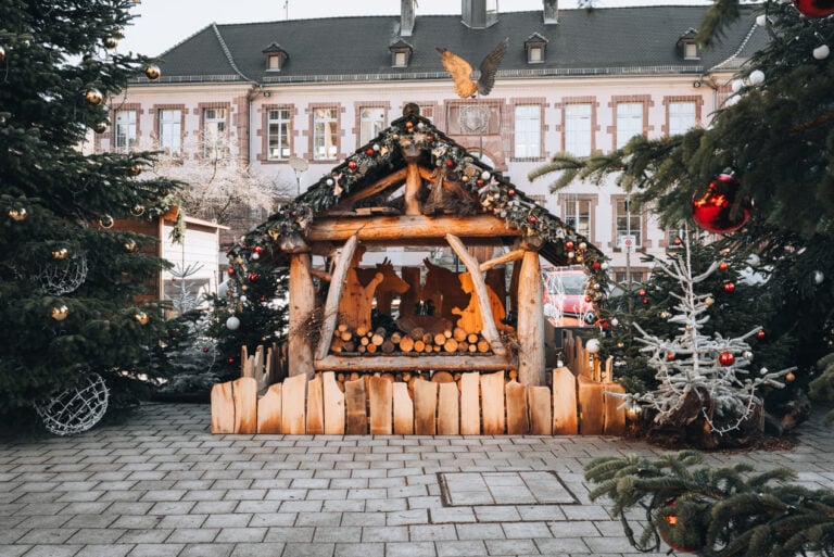 A wooden nativity scene decorated with lights, ornaments, and wreaths sits in Place Joffre at Thann's Christmas Market.