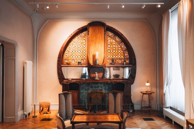 This is the Lounge at the Villa Majorelle. There is a large cabinet with stained glass windows at the back. Then, in front, there is a table and chairs. Each piece has pine cones on it because that is the theme of this room.