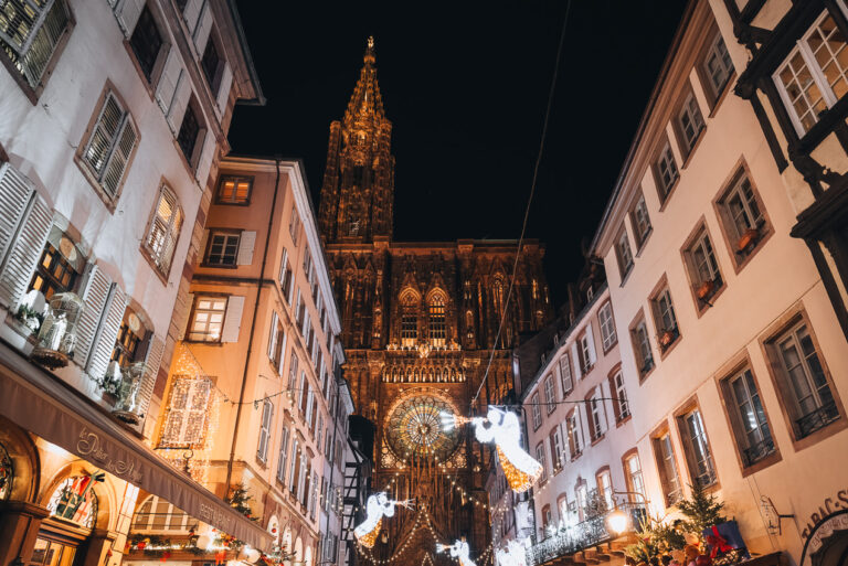 This is the Strasbourg Cathedral at the Strasbourg Christmas Market. It's a night so the decorative lights are on. There are white angles with gold trumpets and the lights of the cathedral are also on.