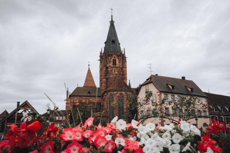 This is the Saint Peter and Saint Paul Abbey in Wissembourg. The photo is taken from the garden so there are flowers in the foreground and the steeple of the church in the background. It's one of the best things to do in Wissembourg.