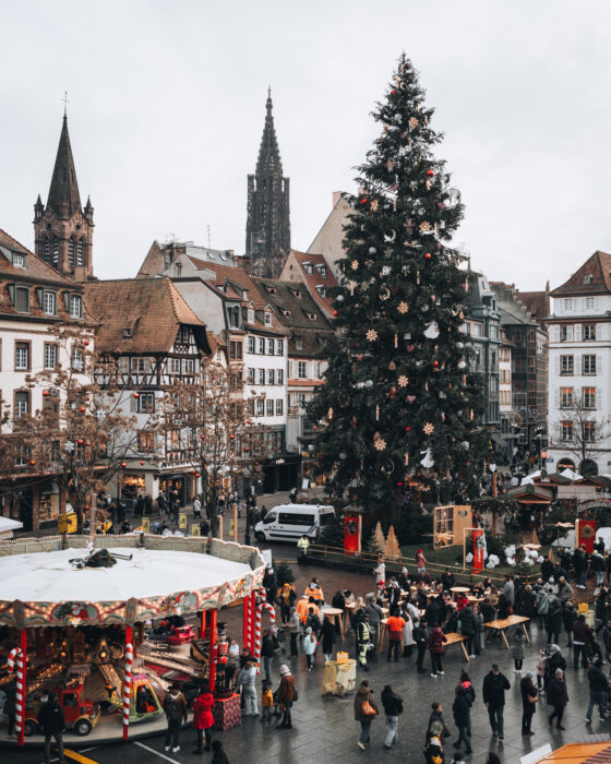 Festive view over Place Kléber in Strasbourg seen from inside the Aubette 1928 building, with a large illuminated Christmas tree glowing in the square below. Holiday lights and decorations fill the surrounding city center, creating a lively winter atmosphere.