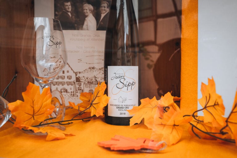 Wine tasting at Jean Sipp winery in Ribeauvillé with a wine glass and a bottle of wine. There are leaves and a table cloth for the setting.
