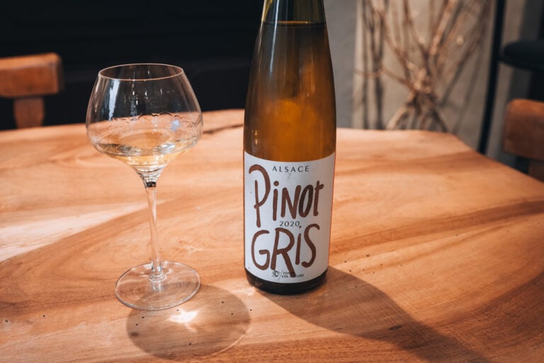 Wine tasting setup at Domaine Martin Jund in Colmar with a glass of wine and a bottle of Pinot Gris on a wooden table.