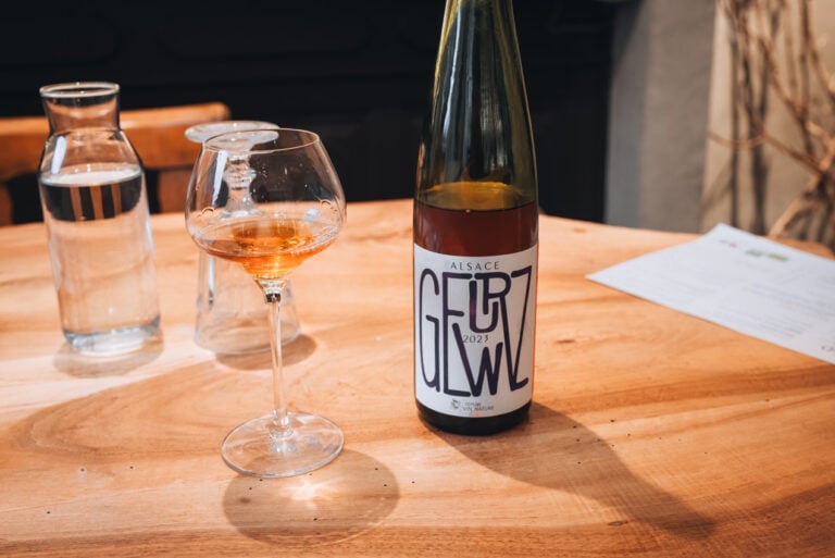 A glass of natural Gewürztraminer wine next to the bottle on a wooden table. This was a part of Jen's wine tasting at Domaine Martin Jund in Colmar.