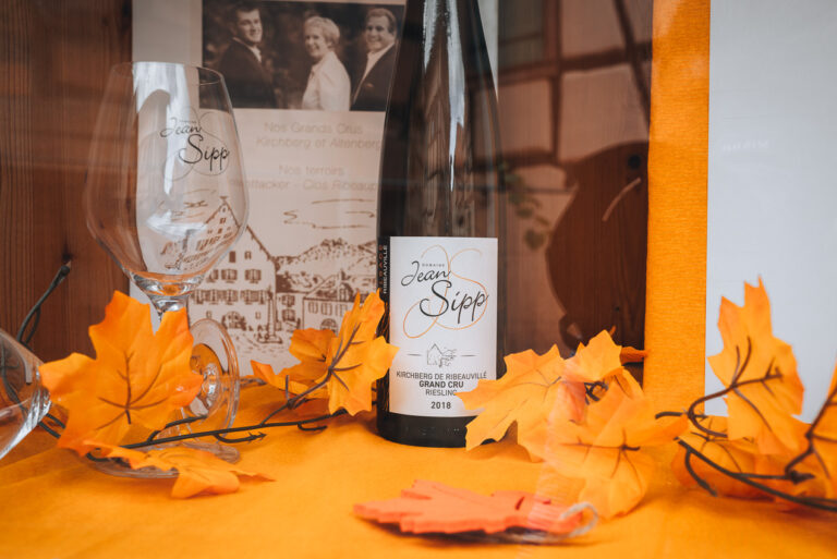 This is a wine bottle from Alsace. There is a wine glass next to the bottle. Wine tasting is popular activity in Eguisheim.