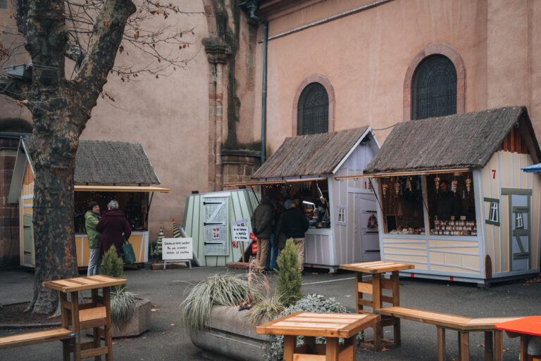 Festive Elf made Wooden Chalets at the Christmas market in Turckheim. Each one is selling local items and there are wooden tables and benches for people to sit.