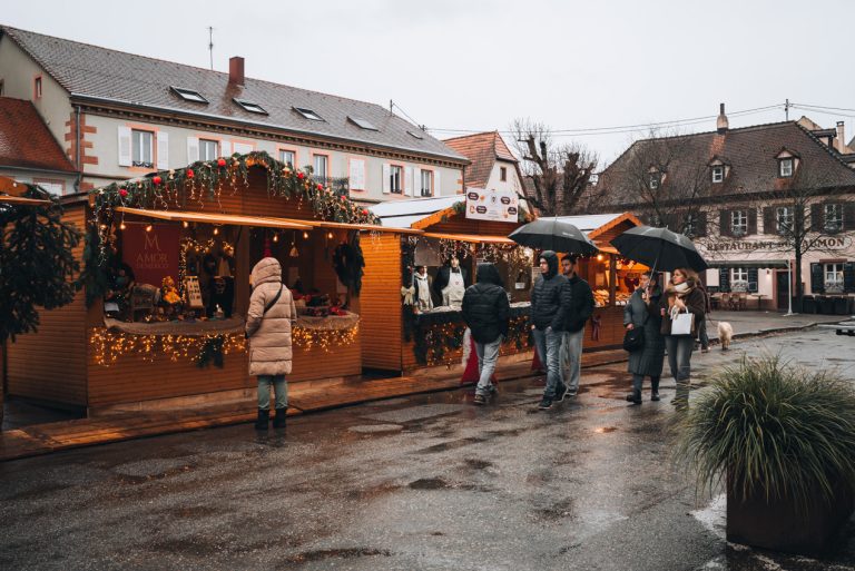 Three wooden chalet in front of the tourist office during the Christmas market in Wissembourg. Each one is selling something different and people are shopping.